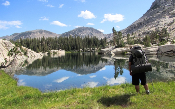 a student stands beside a blue alpine lake reflecting a mountainous landscape